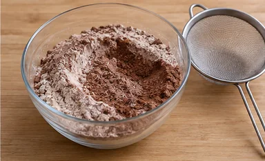 Gâteau au chocolat végétalien : tamiser le cacao avec les poudres — Poudres fines, cacao sans amas.