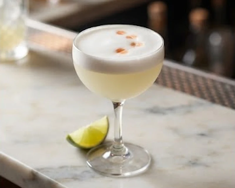 Pisco sour présenté dans son plat de service, avec sa texture et sa garniture visibles